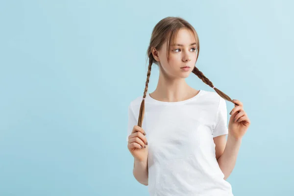 Νέο όμορφο κορίτσι σε λευκό t-shirt κρατώντας δύο μαλλιά πλεξούδες — Φωτογραφία Αρχείου