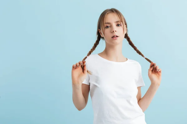 Νεαρό ελκυστικό κορίτσι σε λευκό t-shirt κρατώντας δύο μαλλιά πλεξούδες — Φωτογραφία Αρχείου