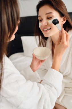 Beyaz bornoz koyu saçlı genç çekici kadın yatakta oturan rüya gibi bir kenara bakarken modern otelde ona kozmetik maske yapmaya yakın güzel kız 