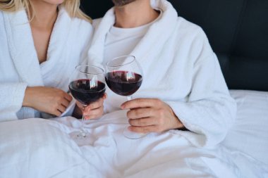 Rahat otelde yatakta yatan elinde kırmızı şarap kadehleri tutan beyaz bornozerkek ve kadın yakın fotoğraf