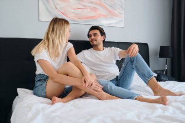 Genç yakışıklı esmer adam rüya gibi güzel sarışın kadın modern otelde birlikte yatakta oturan bakıyor