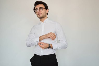 Beyaz gömlek li ve gözlüklü genç esmer adam, beyaz arka plana hayali olarak bakıyor