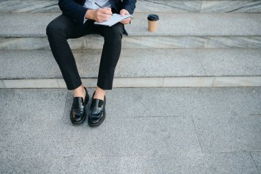 Klasik takım elbiseli yakın adam merdivenlerde açık havada oturan ve writi