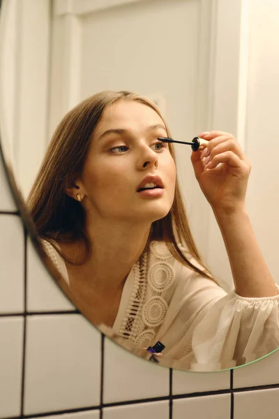 Mladá krásná žena v bílých šatech stojící blízko zrcadlového svalu v koupelně — Stock fotografie