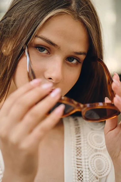 Крупным планом молодая красивая женщина в солнечных очках задумчиво смотрит в камеру на городской улице — стоковое фото