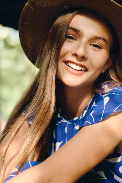 푸른 드레스와 모자를 입고 도시 공원에 앉아있는 카메라를 행복하게 바라보는 예쁜 미소 소녀의 초상화 — 스톡 사진