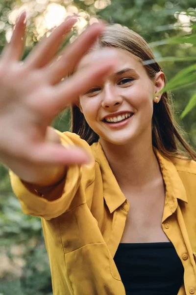 Cerca de la joven hermosa mujer sonriente en camisa amarilla y la parte superior felizmente cubriendo la cámara con la mano en el parque — Foto de Stock