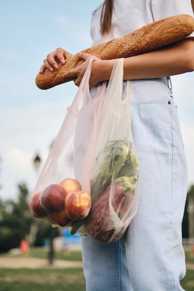 Close-up vrouw staan met stokbrood, perziken en groenten in eco zakken in het stadspark — Stockfoto