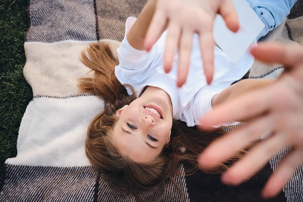 Kaunis hymyilevä teini tyttö makaa ruudullinen onnellisesti vetämällä kädet jopa kameran piknikille puistossa — kuvapankkivalokuva