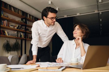 Genç çekici iş arkadaşları mutlu modern ofiste dizüstü bilgisayar ve kağıtları ile yeni proje üzerinde çalışan birbirlerine bakıyor