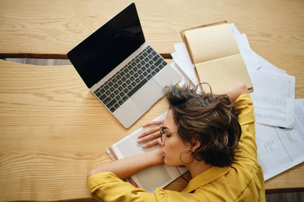 Top view of young tired woman fall asleep on desk with laptop and documents under head at workplace — Stock Photo, Image