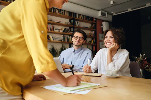 Grupp av leende affärskollegor sitter vid skrivbordet med laptop glatt pratar på jobbet i moderna kontor — Stockfoto