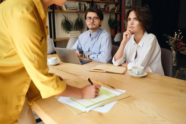 Unga affärskollegor sitter vid skrivbordet med laptop tankfullt titta på Boss med papper i moderna kontor — Stockfoto