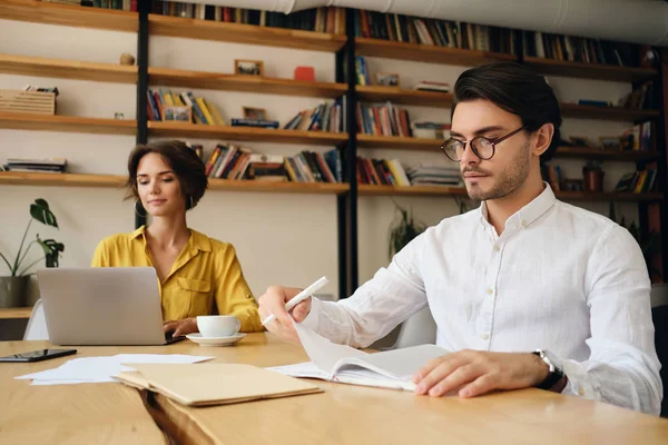 Gözlüklü genç ciddi adam düşünceli arka plan üzerinde meslektaşı ile ofiste çalışan masada oturan — Stok fotoğraf