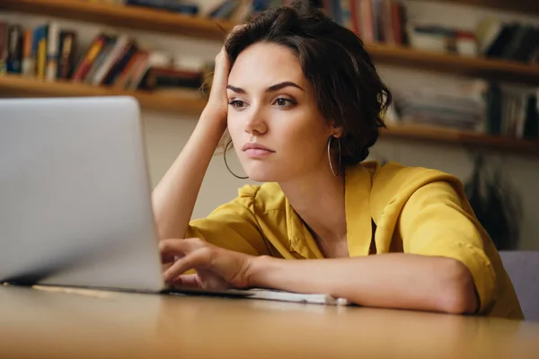 Retrato de una joven mujer de negocios sentada en el escritorio trabajando cansadamente en la computadora portátil en la oficina moderna —  Fotos de Stock