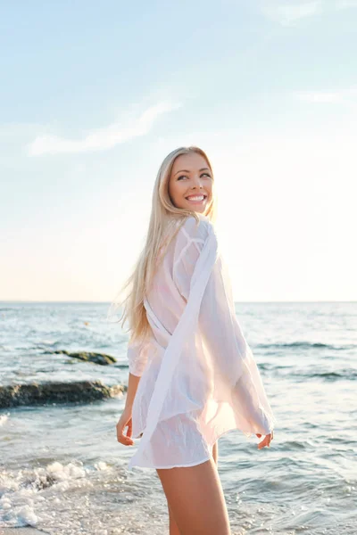 Junge fröhliche blonde Frau in weißem Hemd schaut glücklich beiseite mit schönem Meer auf dem Hintergrund — Stockfoto