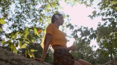 Gün batımında eski bahçede hayali bir şekilde ağaç dalı üzerinde oturan saç çiçekli güzel latin kız çekim izleme