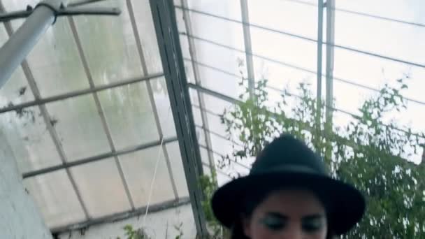 帽子和皮夹克的有吸引力的女孩的概念拍摄自信地看着在温室的相机 — 图库视频影像