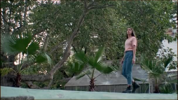 跟踪周围拍摄的有吸引力的女孩在T恤和牛仔裤梦想走在老花园与热带叶子的背景 — 图库视频影像