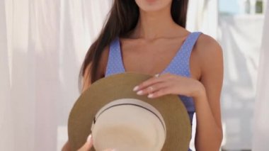 Şapka ile mayo güzel esmer kız romantik çekim düşünceli kamera bakıyor ve deniz kenarında perdeler ile oynarken