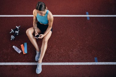 Stadyumda egzersiz sonrası dinlenen cep telefonu ile spor giyim çekici sportif kız Üst görünümü