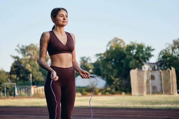 Hermosa chica de fitness en ropa deportiva con estilo con saltar la cuerda de entrenamiento de ensueño en el estadio de la ciudad —  Fotos de Stock