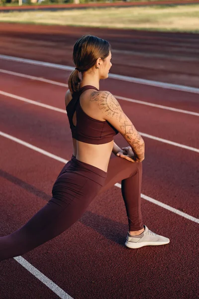Attraente ragazza sportiva in abbigliamento sportivo facendo esercizi di stretching durante l'allenamento sullo stadio della città — Foto Stock
