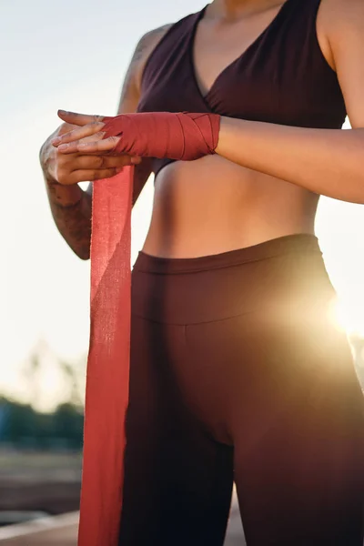 Close up menina esportiva em sportswear elegante envolvendo bandagem de boxe vermelho na mão no estádio — Fotografia de Stock