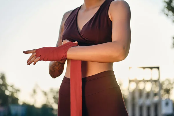 De cerca chica atleta en ropa deportiva envolviendo vendaje de boxeo rojo en la mano en el estadio —  Fotos de Stock