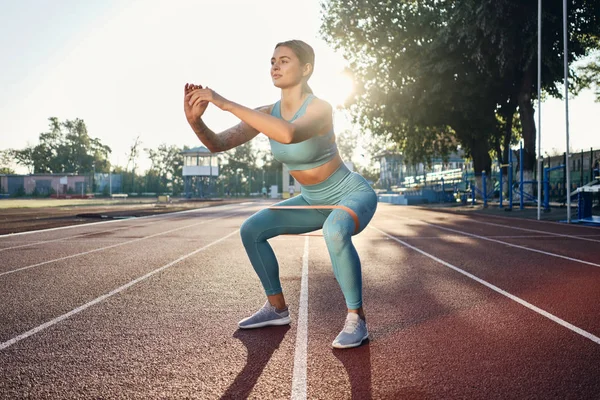 Красива спортивна дівчина в стильному спортивному одязі з гумкою під час тренування на міському стадіоні — стокове фото