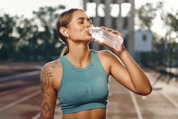 Atrakcyjna sportowa dziewczyna w Sportswear szczęśliwie wody pitnej po treningu na stadionie miejskim — Zdjęcie stockowe