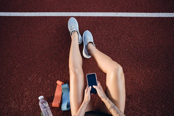 Pohled na sportovní dívku s mobilními telefony po cvičení na stadionu — Stock fotografie