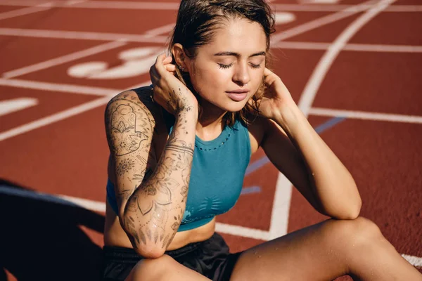 Menina atleta molhado atraente em sportswear sonhadoramente descansando após o treino no estádio da cidade — Fotografia de Stock