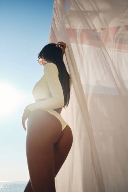 Şeffaf perdeler ile plaj yatağında güneşlenme mayo güzel ince esmer kız Arka görünümü