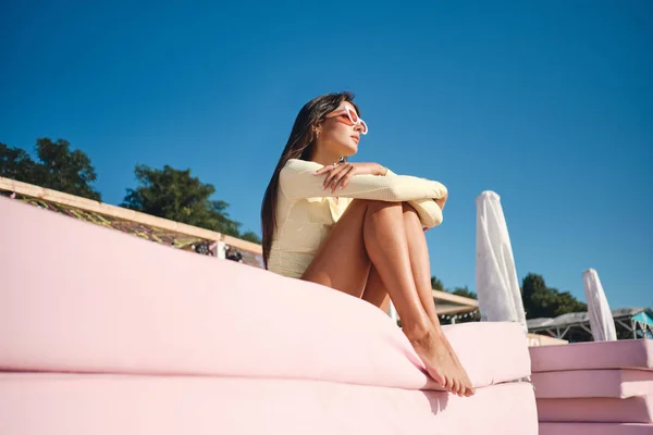 Belle fille brune romantique en maillot de bain et lunettes de soleil colorées reposant de rêve sur un lit de plage rose — Photo