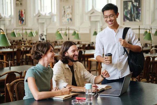 Grupa młodych radosnych studentów z radością rozmawia studiując w bibliotece Uniwersytetu — Zdjęcie stockowe