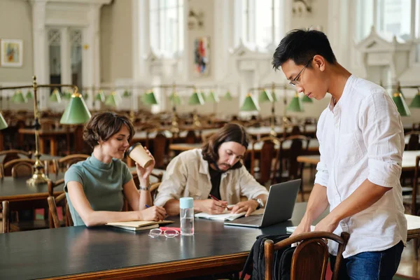 Giovane asiatico maschio studente in occhiali con zaino venire a studiare con gli amici in biblioteca di università — Foto Stock