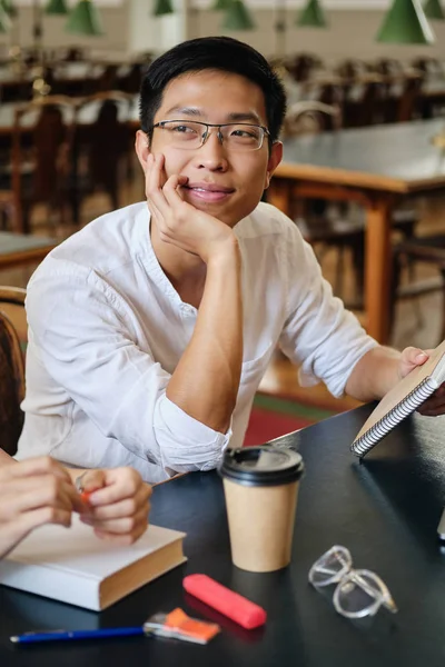 Młody atrakcyjny Asian męski student w okulary dreamily studiowanie w Biblioteka z Uniwersytet — Zdjęcie stockowe