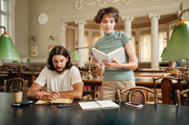 Üniversite kütüphanesinde ders sırasında genç öğrenciye yeni tema açıklayan kitap ile Çekici kadın öğretmen