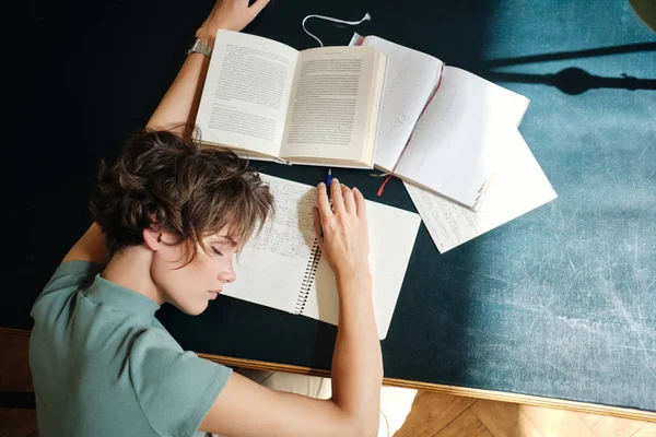 Visão superior da jovem estudante exausta do sexo feminino cansadamente dormindo na mesa com livros e resumo durante o estudo na biblioteca da universidade — Fotografia de Stock