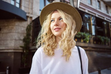 Şapkalı çekici rahat sarışın kız portresi hayali şehir caddesinde yürürken uzağa bakıyor