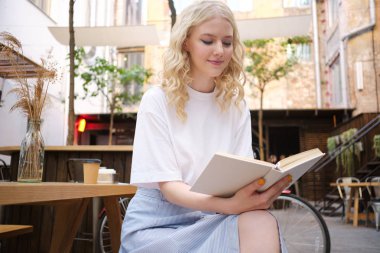 Güzel romantik sarışın kız rüya kafenin avlusunda kitap okuma  