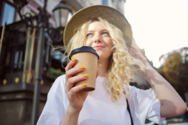 Fuzzy retrato de atractiva chica rubia casual en sombrero soñando con mirar hacia otro lado con café para ir en la mano en la calle de la ciudad —  Fotos de Stock