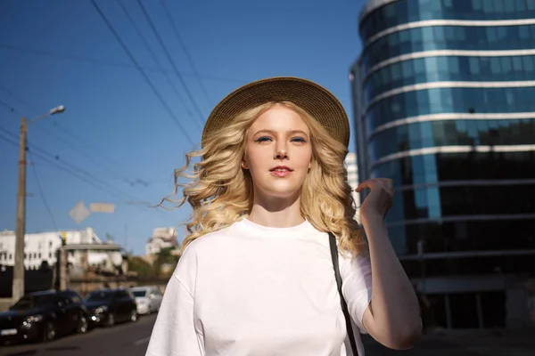 Красивая блондинка в шляпе задумчиво смотрит в камеру на городской улице — стоковое фото