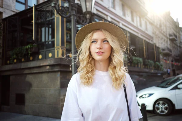 Retrato de menina loira casual em chapéu sonhadoramente andando na rua da cidade. Jovem mulher bonita de pé ao ar livre — Fotografia de Stock