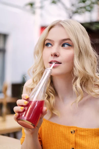 Портрет красивой мечтательной блондинки, задумчиво глядящей в сторону и пьющей лимонад во дворе кафе — стоковое фото
