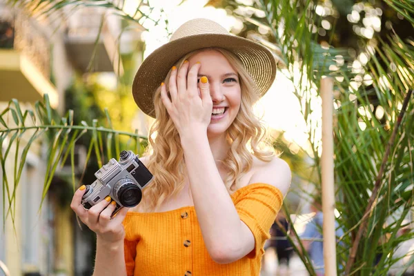 Belle fille blonde romantique en chapeau tenant joyeusement caméra rétro à la main sur la rue de la ville — Photo