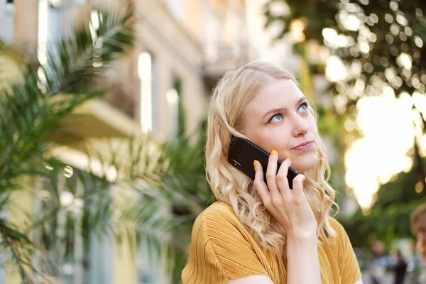 Portrait de fille blonde ennuyée regardant pensivement loin parler sur un téléphone portable dans la rue de la ville — Photo