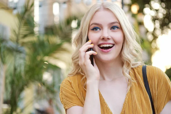 Portrait of beautiful joyful blond girl happily talking on cellphone outdoor — Stok Foto