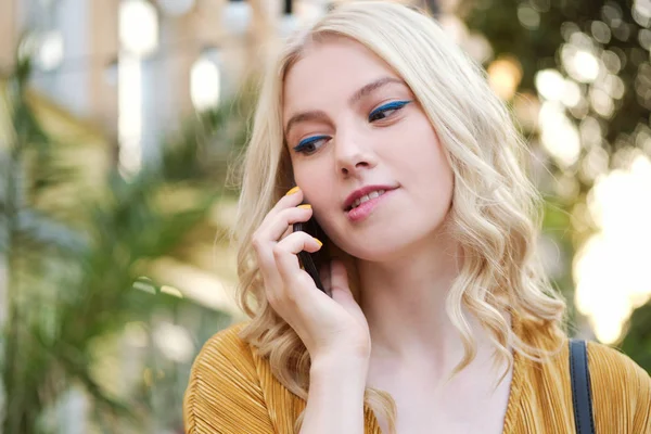Портрет красивой кокетливой блондинки, мечтательно разговаривающей по мобильному телефону на открытом воздухе — стоковое фото